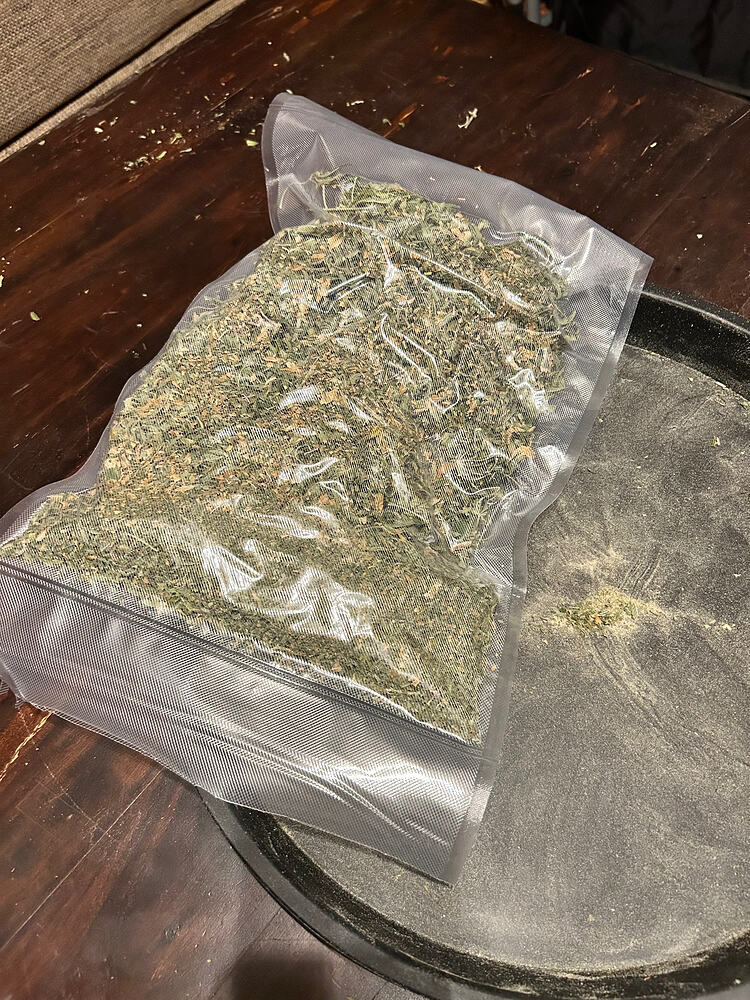 Ein vakuumierter Beutel mit Cannabis-Schnittresten oder Popcorn-Buds auf einem dunklen Tablett.