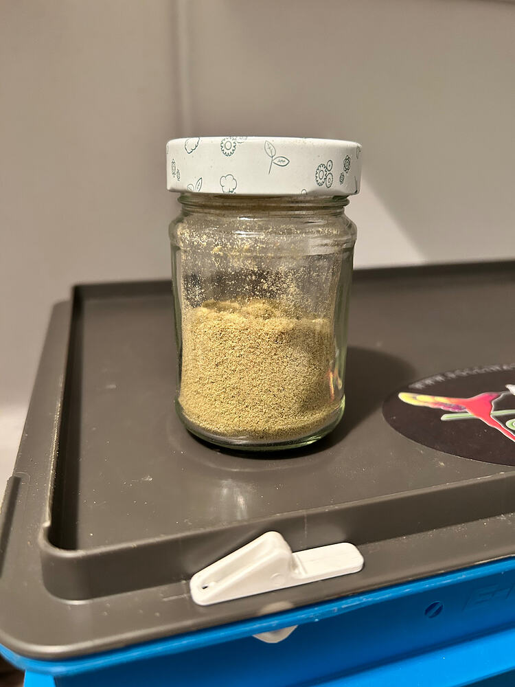 Ein kleines Glas gefüllt mit hellem, pulverförmigem Cannabis-Kief, das auf einer grauen Ablage steht.