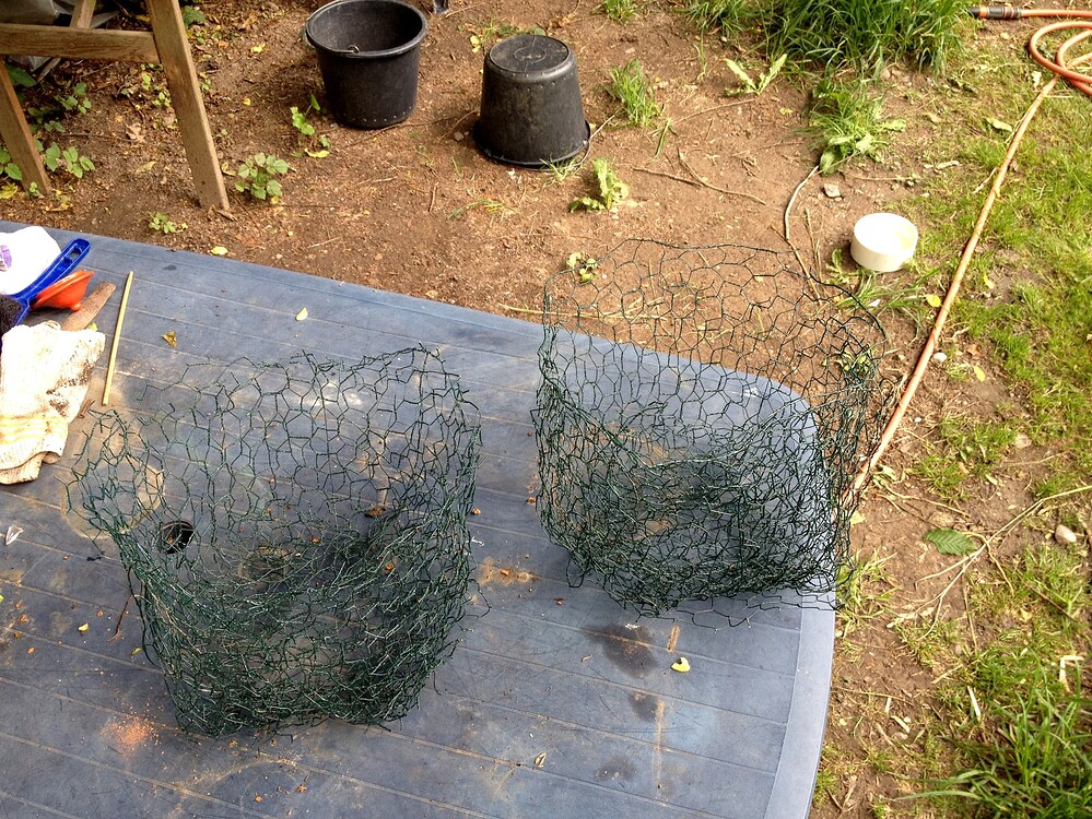 Zwei aus Drahtgeflecht selbstgebaute Körbe auf einer blauen Kunststoffoberfläche im Garten, vorbereitet als Schutz gegen Wühlmäuse.