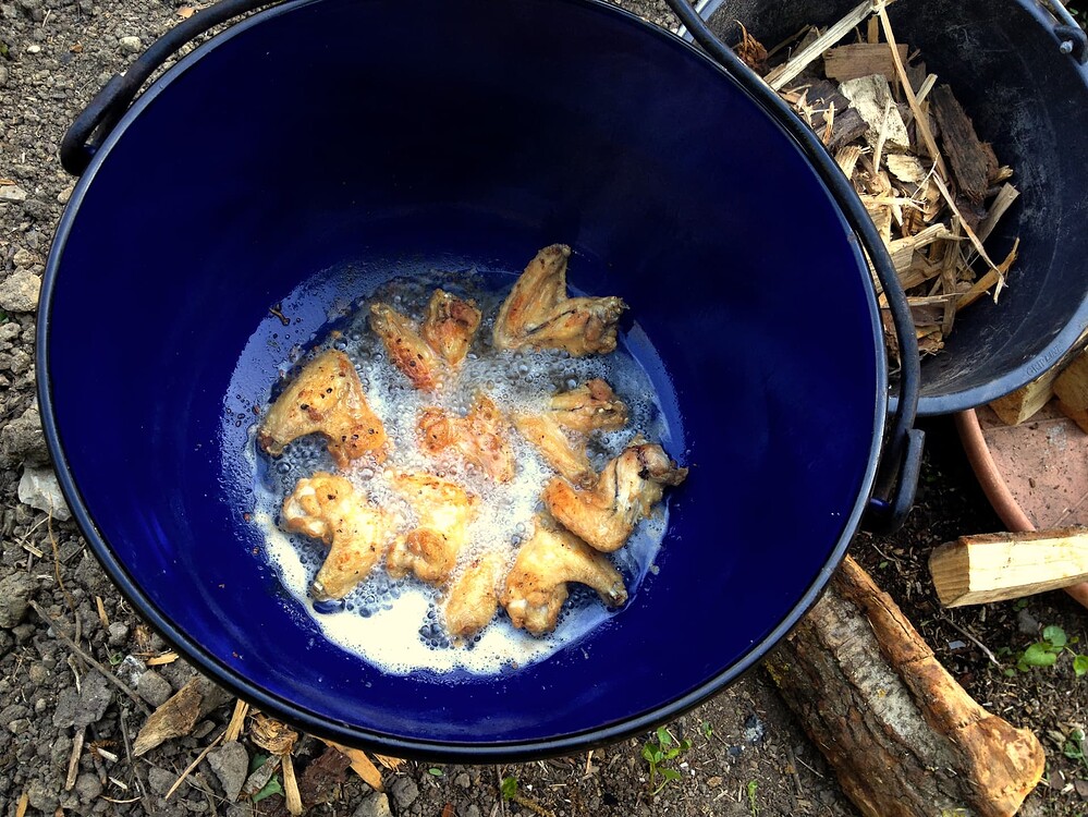 Ein blauer Topf über einem Feuer, in dem Chicken Wings in heißem Fett gebraten werden.