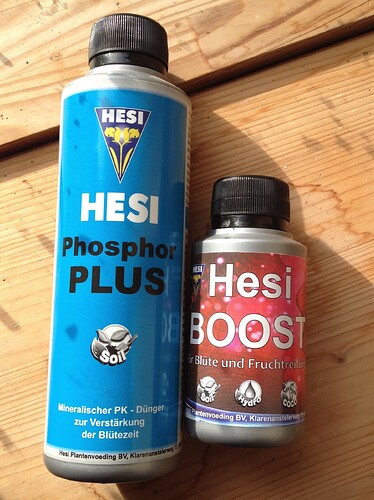 Zwei Flaschen Hesi Dünger, Phosphor Plus und Hesi Boost, stehen auf einer Holzoberfläche.