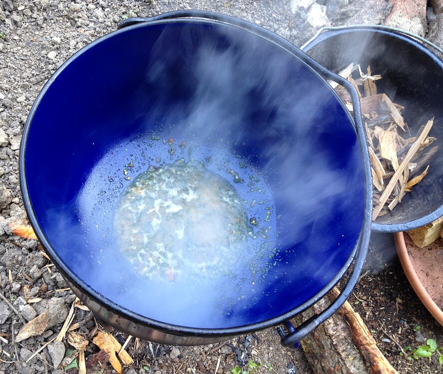 Ein blauer gusseiserner Topf über einem offenen Feuer, in dem Bratensatz abgelöscht wird.