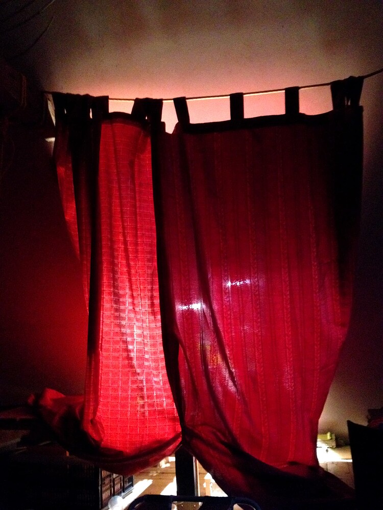Rote Vorhänge vor einem Fenster, durch die rötliches Licht scheint.