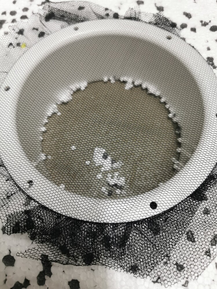 Ein weißer Abluftflansch, der in eine Styroporplatte eingelassen und mit einem schwarzen Fliegennetz bespannt ist.
