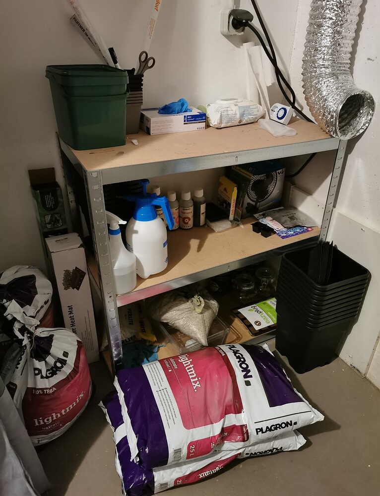 Ein Metallregal in einem Raum, gefüllt mit Grow-Equipment wie Plagron Light Mix Erde, Töpfen, Sprühflaschen und Düngemitteln.